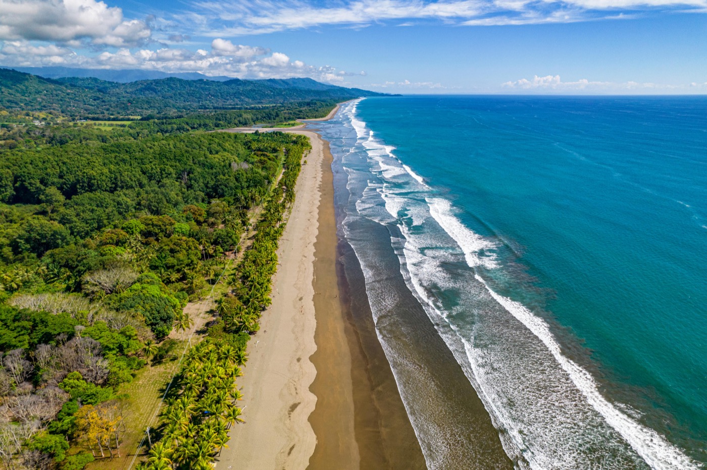 A sweeping aerial view of a Costa Rica beach lined with jungle and bright blue water.